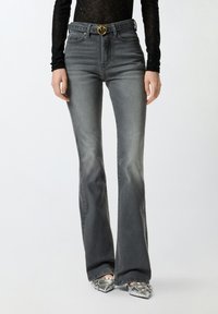 Jeans acampanados de color gris oscuro con cintura alta, que cuentan con un hebilla de cinturón dorada, bolsillos frontales y un ligero efecto de decoloración.