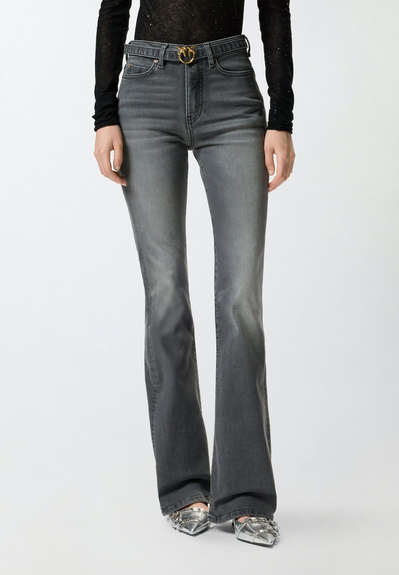 Jeans acampanados de color gris oscuro con cintura alta, que cuentan con un hebilla de cinturón dorada, bolsillos frontales y un ligero efecto de decoloración.