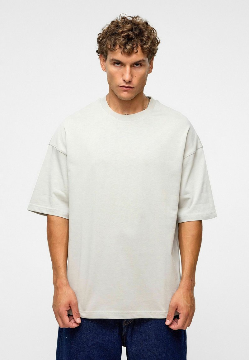 T-shirt oversized gris clair à manches courtes, col rond, texture douce et ourlet droit, associé à un pantalon en denim bleu.