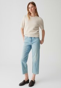 Lichtbeige kortom mouwensweater, zachte textuur; gecombineerd met lichtblauwe cropped jeans en donkerbruine loafers.