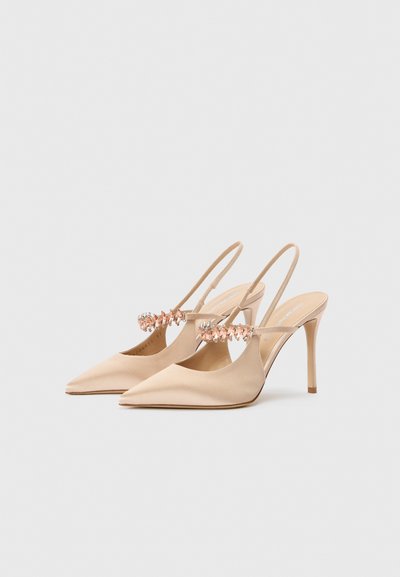 Beżowe szpilki typu slingback z zakończonymi w szpic noskami, cienkim obcasem typu szpilka i ozdobnymi kryształowymi aplikacjami na cholewce.