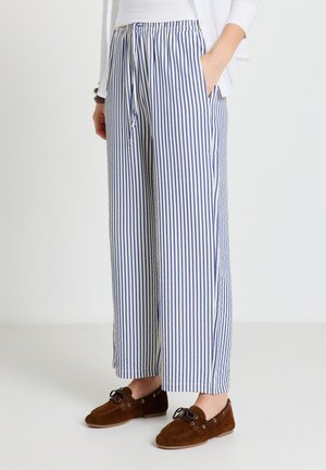 Persona che indossa pantaloni larghi a righe verticali bianche e blu con coulisse e mocassini marroni in camoscio con lacci.