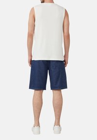Weißes ärmelloses Oberteil kombiniert mit dunkelblauen Jeansshorts. Das Outfit wird mit weißen Sneakers abgerundet. Einfaches Design und lässige Passform.