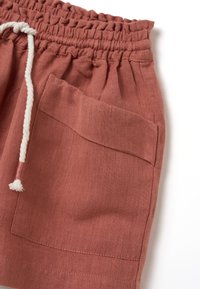 Shorts couleur rouille en tissu texturé avec une taille élastique, un cordon de serrage, et une grande poche latérale pour le rangement.