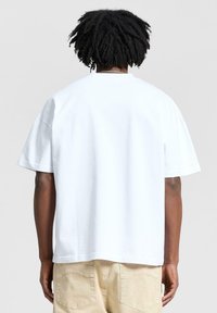 Valkoinen puuvillapaita, jossa on rento istuvuus, lyhyet hihat ja suora helma. Minimalistinen muotoilu ilman graafisia elementtejä tai kuvioita.