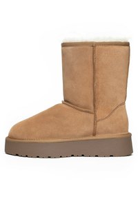 Bota de ante color marrón claro hasta el tobillo con punta redonda, suave forro de piel sintética blanca en la parte superior y suela de goma texturizada para mayor tracción.