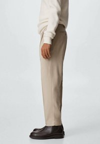 Pantaloni beige su misura con gamba dritta, realizzati in tessuto morbido. Abbinati a stivali alla caviglia marrone scuro, con un design sobrio.