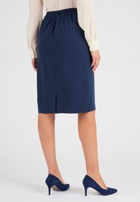 Jupe crayon navy avec taille élastique, longueur genou, comportant une fente au centre à l'arrière et associée à des talons hauts en daim bleu foncé.
