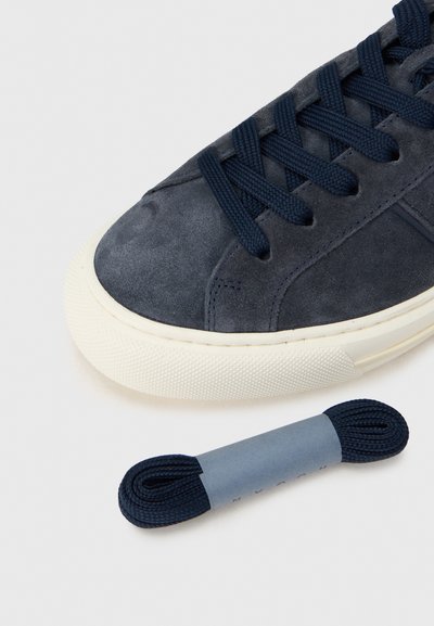 Ναυτικό σουέντ αθλητικό παπού τσι με επίπεδα ναυτικά κορδόνια και υφασμένο κρεμ λάστιχο σόλα. Περιλαμβάνει επιπλέον ζευγάρι ναυτικά κορδόνια τυλιγμένα με χαρτονένια ταινία.