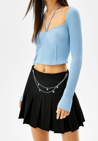 Světle modrý žebrovaný cropped top s dlouhými rukávy a čtvercovým výstřihem, který je spárován s černou skládací sukní s doplňkem v podobě stříbrného řetízku.