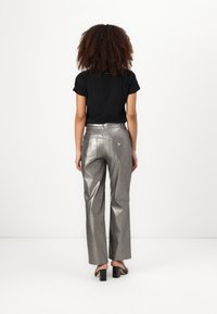 Metallic silver wide-leg pants with a smooth texture, pocket details, and a small logo on the back, paired with a black short-sleeve shirt.