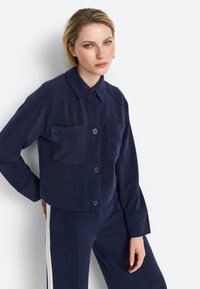 Navy blue cropped jacket in a soft fabric, featuring a button-up front, two chest pockets, and long sleeves with a relaxed fit.