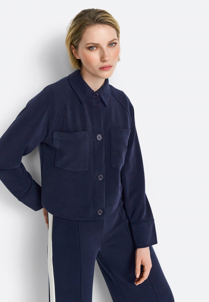 Navy blue cropped jacket in a soft fabric, featuring a button-up front, two chest pockets, and long sleeves with a relaxed fit.