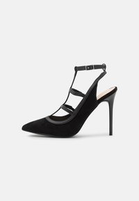 Sandalhe de salto alto em camurça preta com bico fino, costas abertas e vários detalhes em tiras; apresenta um salto preto brilhante e elegante.