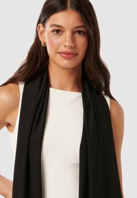 Black pleated scarf made of lightweight fabric, draped around the shoulders, with a smooth texture and a modern design.