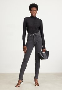 Black long-sleeve top with ruching, paired with high-waisted dark gray skinny jeans, and a small black handbag. High-heeled black sandals.