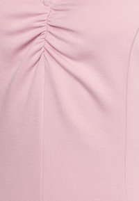 Tecido rosa claro com uma superfície texturizada e em relevo. Apresenta detalhes gathered no centro, criando um caimento subtil.