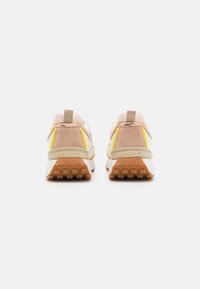 Sport shoes in light pink and beige, featuring mesh and suede materials, rubber sole, and yellow accents. Back view with logo detail.