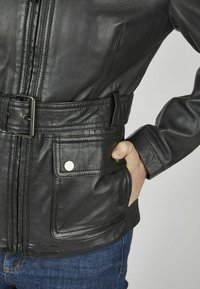 Zwarte leren jas met een geïnspireerde taille, ritsluiting en zijzakken. Zachte textuur met stikdetails en metalen drukkers.