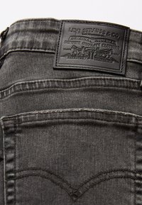 Zadní kapsa tmavě šedých džínsů Levi Strauss z denimu s černou koženou značkovou nášivkou s embosovaným logem a textem.