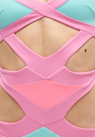 Back view of clothing with pink and blue fabric cutouts revealing skin with a small mole on the right side.