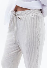 Lichtgrijze gestreepte broek met een trekkoord in de taille en zijzakken. Het materiaal lijkt zacht, met een gladde textuur en een subtiel patroon.