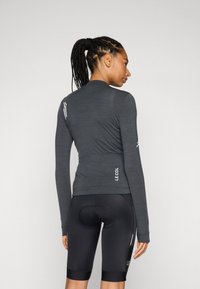 Langermet, mørkegrå sykkeltrøye med en tettsittende design, strukturert stoff og 'LE COL'-merke på baksiden. Kombinert med svarte polstrede shorts.