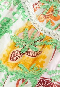 Tissu blanc avec broderies florales colorées en vert, orange et rouge. Présente un col en dentelle et divers motifs de feuilles.