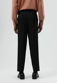 Zwarte broeken met een rechte pasvorm, voorzien van zijzakken, ceintuurlussen en subtiele plooien, gecombineerd met een bruin langärmelig shirt met textuur.