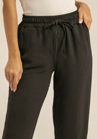 Pantalons noirs à taille élastique en tissu texturé, avec poches avant et détail de cordon de serrage. Silhouette ajustée et ample.