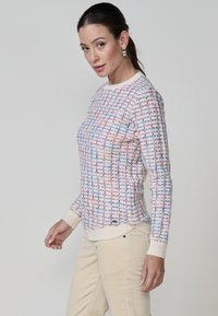 Pull en tricot avec un motif texturé en crème, bleu et rouge. Manches longues et poignets côtelés. Design ajusté avec un ourlet incurvé.