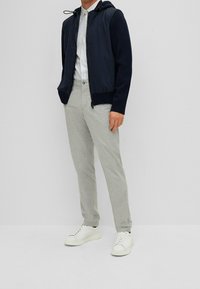 Marinblå huvtröja med dragsko, grå byxor och vita sneakers. Har en dragkedja fram och ribbade ärmslut. Avslappnad stil.