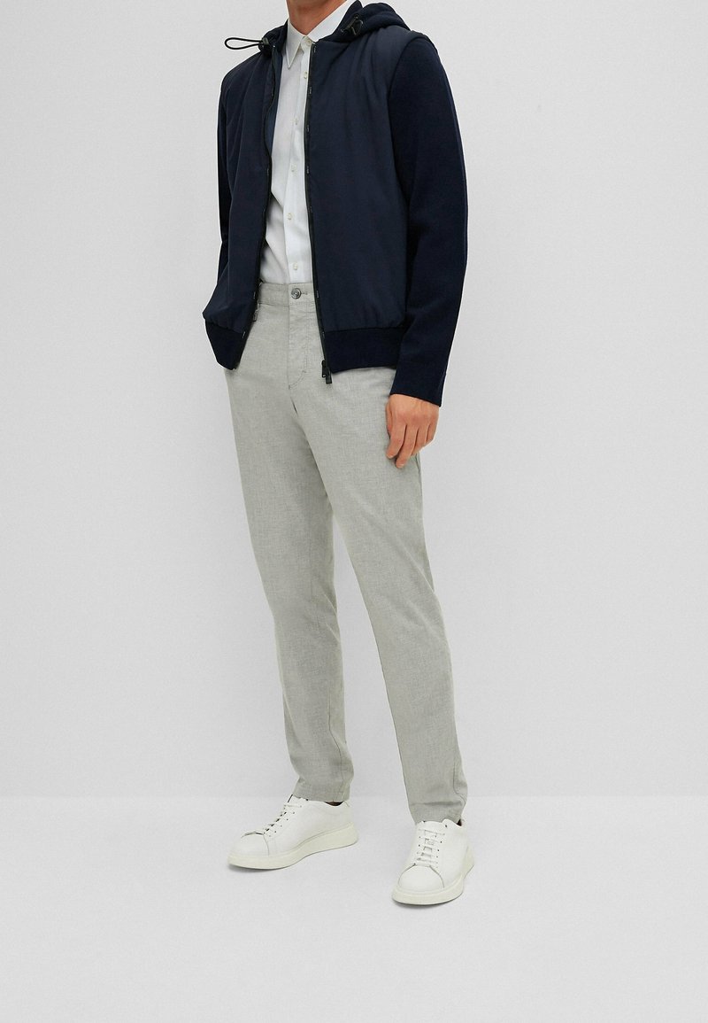 Marinblå huvtröja med dragsko, grå byxor och vita sneakers. Har en dragkedja fram och ribbade ärmslut. Avslappnad stil.