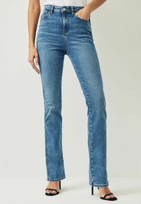 Höga blå denimjeans med raka ben, subtila blekningar och sömnadsdetaljer. Bärs med svarta remsandaler med hög klack.