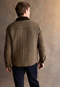 Brown checkered jacket with a corduroy collar, textured fabric, long sleeves, and a straight cut, paired with dark trousers.