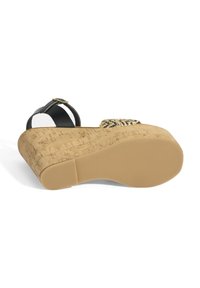 Sandale noire avec plate-forme en liège, présentant une surface texturée beige et un accent tissé noir et beige. Bride réglable avec boucle dorée.