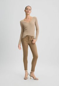 Beige pikad varrukad ribatop, millel on V-kaelus, kombineerituna tihedalt istuvate pruunide teksade ja rihmaga metallik kõrge kontsaga sandaalitaga. Ühtlane tekstuur kogu ulatuses.
