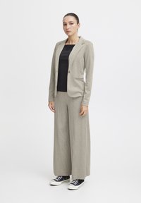 Beige checkered suit with a fitted blazer and wide-leg trousers, paired with a black top and black sneakers. Smooth texture, structured design.