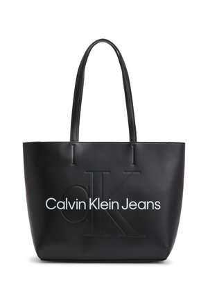 Czarna torba typu tote z wytłaczanym dużym logo "CK" i białym napisem "Calvin Klein Jeans", wyposażona w dwa długie uchwyty.