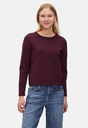 Maglione bordeaux a maniche lunghe con scollatura rotonda e dettaglio a fiocco all'orlo, realizzato in un materiale morbido, abbinato a jeans in denim blu.