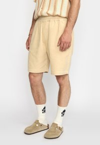 Beige corduroy shorts met een elastische tailleband. Gecombineerd met crèmekleurige sokken met een grafisch ontwerp en tan kleurige suède instappers.