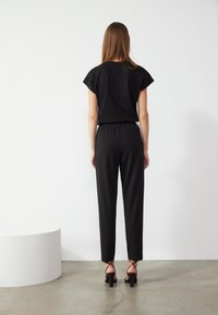 Czarny top z krótkim rękawem w połączeniu z czarnymi zwężającymi się spodniami. Outfit ma luźny krój i jest uzupełniony o czarne sandały na obcasie.