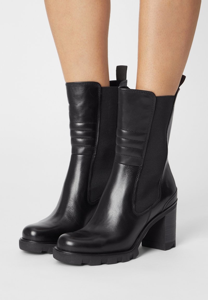 Bottines en cuir noir avec des panneaux élastiques sur les côtés, des accents texturés et un talon épais. Fini lisse avec une semelle en caoutchouc à rainures.