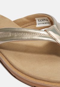 Infradito metallici dorati con una morbida soletta in suede beige e suola in gomma testurizzata, caratterizzati da una fascetta cucita e un'etichetta campione.