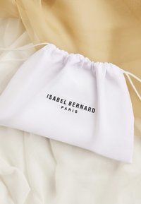 Witte trekkoord zak met zwarte tekst "ISABEL BERNARD PARIS", gemaakt van zachte stof, met een gladde textuur.