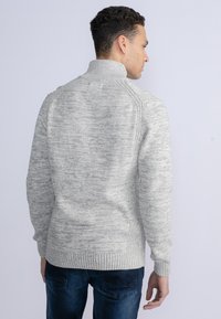 Maglione grigio testurizzato con colletto alto, polsini e orlo a costine; presenta un sottile motivo mélange. La vista posteriore mostra una vestibilità rilassata e dettagli lavorati a maglia.