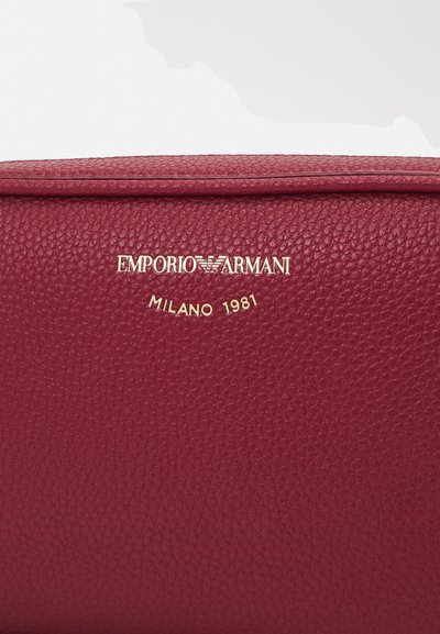 Portafoglio in pelle rossa con superficie testurizzata, caratterizzato dal logo dorato "Emporio Armani" e dall'iscrizione "Milano 1981". Design piatto con bordi netti.