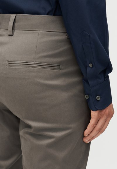 Άνδρας που φοράει γκρι παντελόνι με πίσω τσέπη και μπλε σκούρο πουκάμισο με κουμπιά, ο μανίκι του οποίου φαίνεται δίπλα του.