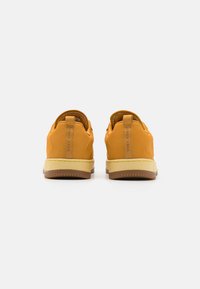 Baskets en cuir jaune avec un dos texturé, un col rembourré et une semelle en caoutchouc avec un accent marron contrastant.