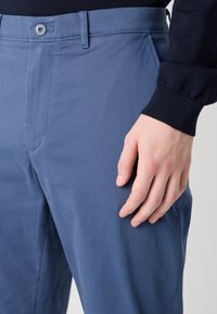 Pantaloni in cotone azzurro chiaro, svasati, con tasche frontali, chiusura a bottoni e una texture liscia. La vita è piatta con passanti per cintura.